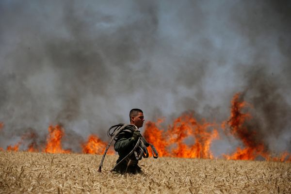 An Israeli soldier carries a hose as he walks in a burning field on the Israeli side of the border fence between Israel and G