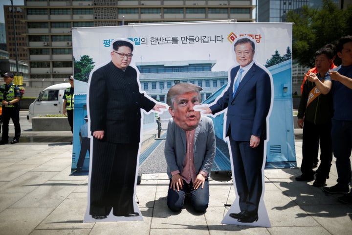 A man wearing a Trump mask kneels between cutouts of North Korean leader Kim Jong Un and South Korean President Moon Jae-in during an anti-Trump rally in Seoul, South Korea, on May 25, 2018. 