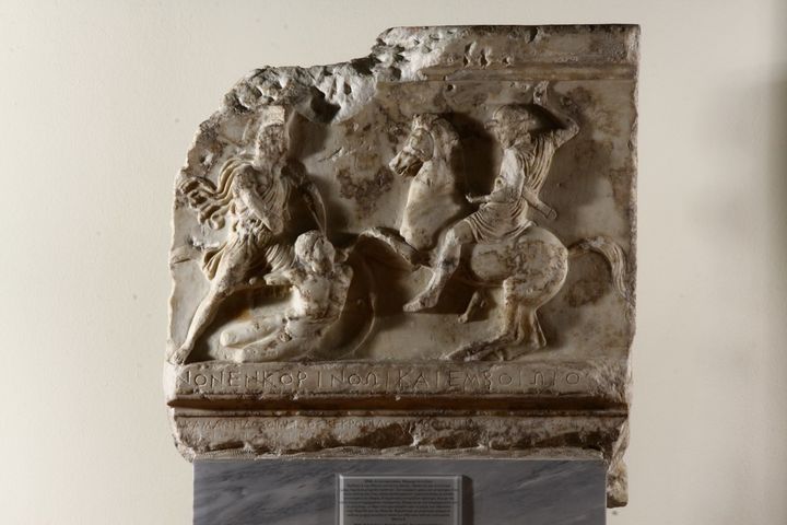 Άνω τμήμα του επιτυμβίου μνημείου που έστησαν οι Αθηναίοι για να τιμήσουν τους πεσόντες στις μάχες της Κορίνθου και της Κορώνειας το 394 π.Χ. Βρέθηκε στο Δίπυλο το 1907. Στον κανόνα κάτω η επιγραφή ΑΠΕΘΑ]ΝΟΝ ΕΝ ΚΟΡΙΝΘΩΙ ΚΑΙ ΕΝ ΒΟΙΩΤΟΙ[Σ]. Στον κορμό της στήλης είναι χαραγμένα τα ονόματα των πεσόντων και οι φυλές τους.