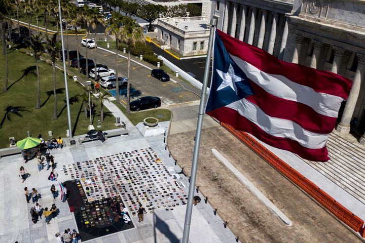 A Puerto Rican flag flies above empty pairs of shoes outside the island's Capitol building.