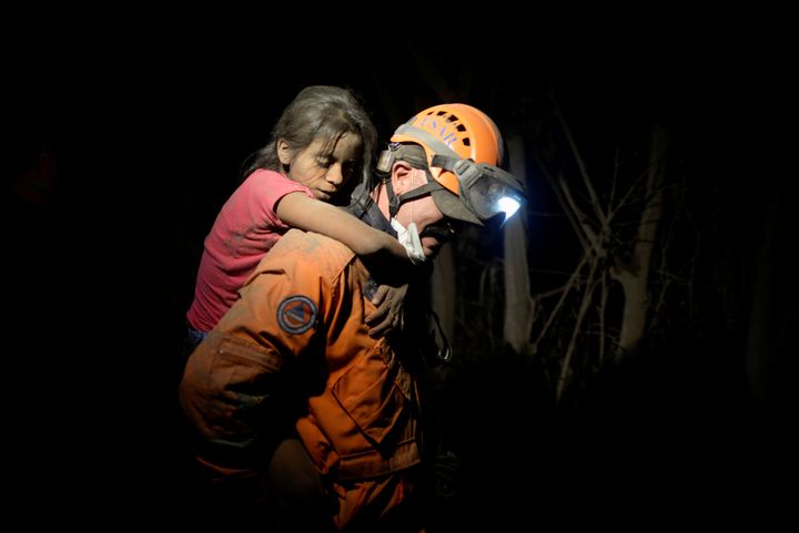 A rescue worker carries a child covered with ash 