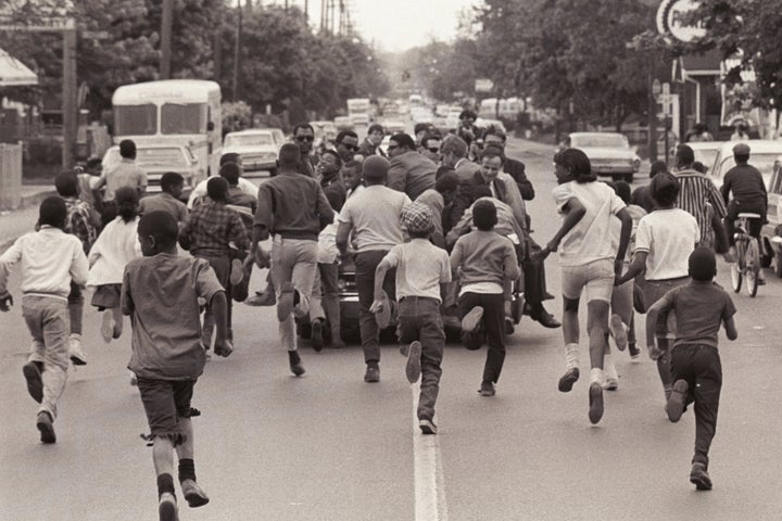 A group of children run after an open-top convertible carrying Kennedy, then a senator from New York, as he campaigned f
