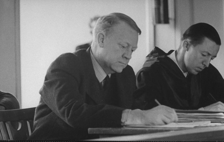 Vidkun Quisling (left) jotting down a note during trial.