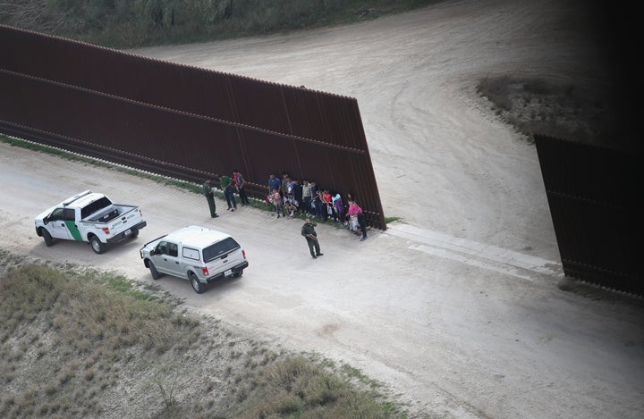 U.S. Border Patrol agents stand with undocumented immigrant families at the U.S.-Mexico border fence before transporting them