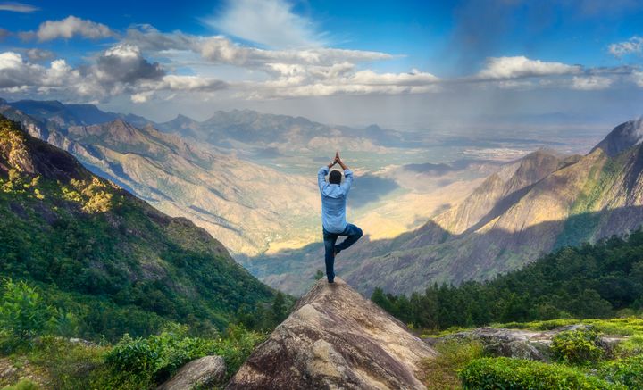 Man doing yoga on the peak of a mountain in Tamilnadu, India.
