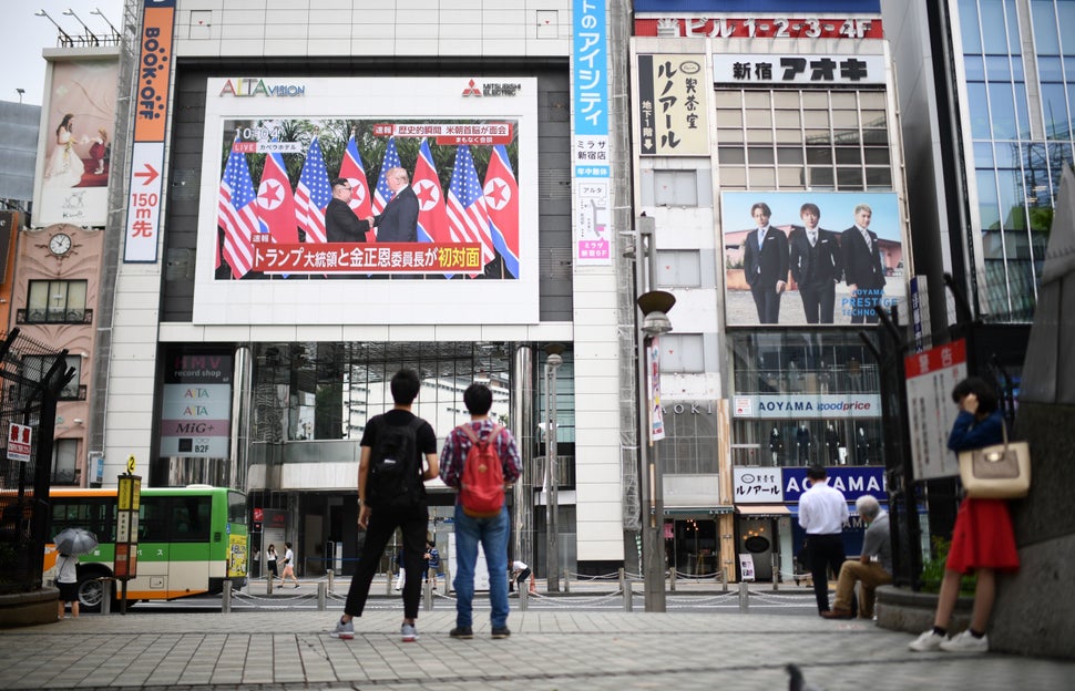 Pedestrians in Tokyo look at a wall-mounted screen displaying live news of the meeting between Trump and Kim on June 12, 2018