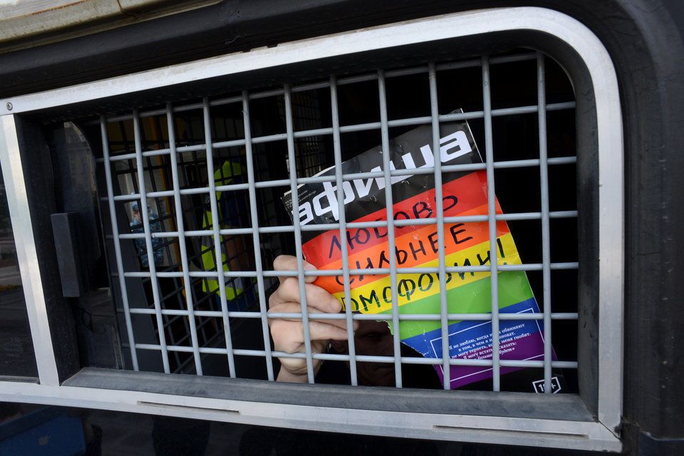 An unknown gay-rights activist in a police vehicle in Moscow. His sign says: 'Love is stronger than homophobia'.
