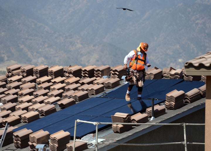 Workers install solar panels on the roofs of homes under construction south of Corona, California.