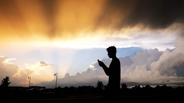 <p>A teenage boy checks his cellphone as a storm approaches. Teen depression and suicide rates are rising sharply. Some research indicates social media and excessive use of online devices may be a cause.</p>