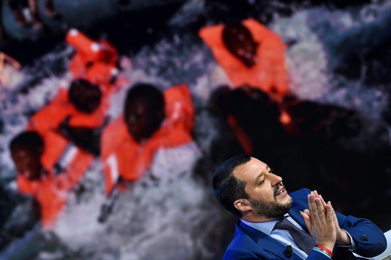 Italy's Interior Minister and Deputy Prime Minister Matteo Salvini speaks on an talian talk show as picture of migrants is displayed in the background.