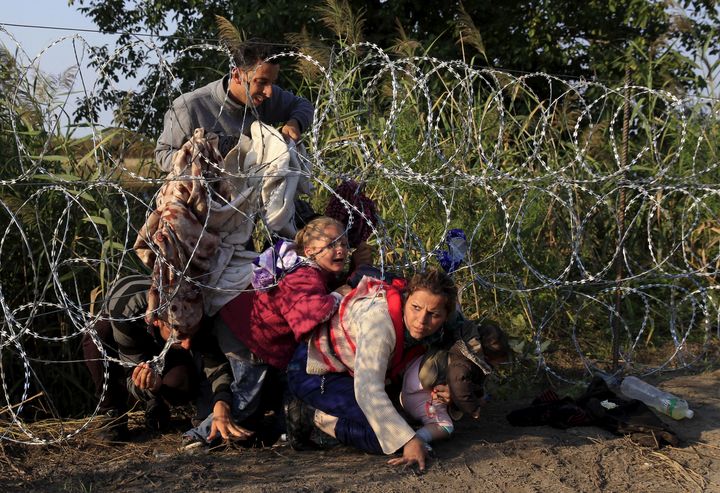 Syrian migrants cross under a fence as they enter Hungary at the border with Serbia on Aug. 27, 2015.