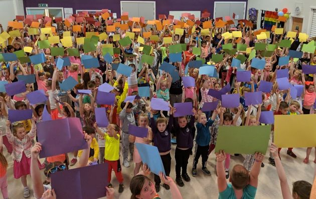 Children at Downfield Primary School hold up coloured card to make a 400-person rainbow flag.