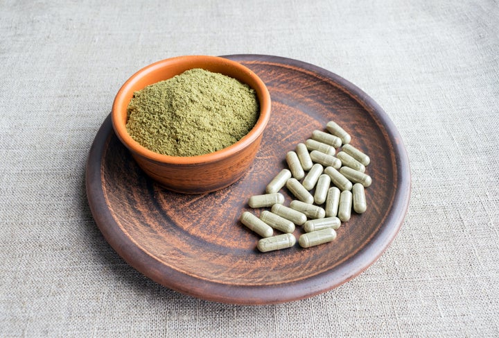 Kratom powder is seen next to capsules containing the herbal supplement.