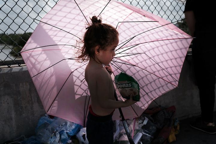 A Honduran child stands in the shade of an umbrella as she waits with her mother along the border bridge after being denied e