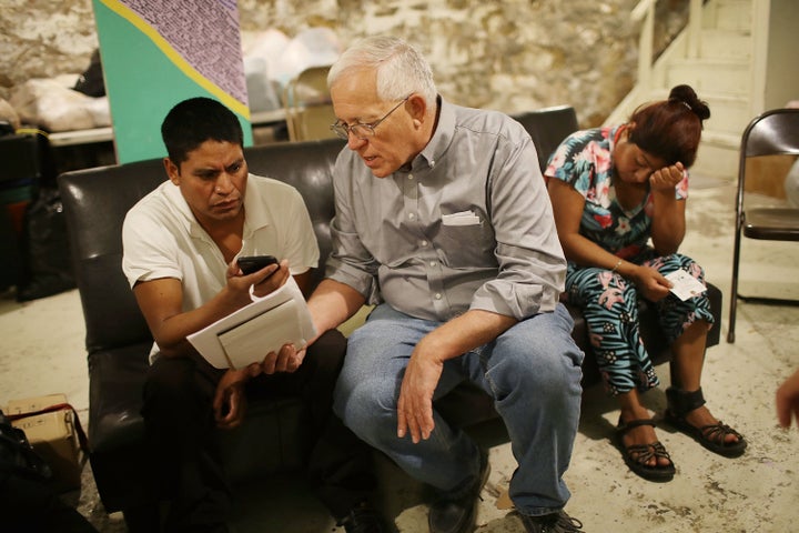 Ruben Garcia (center), director of Annunciation House, speaks on a cellphone with a person from the Office of Refugee Resettlement as he sits with two migrants, Josue (left) and Miriam (right), who are trying to track down their children after being released from U.S. Customs and Border Protection custody on June 25, 2018, in El Paso, Texas.