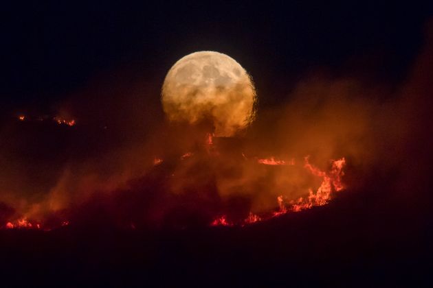 The full moon rises behind burning moorland 