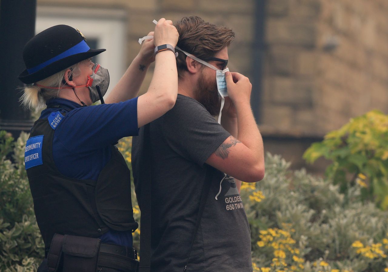 A PCSO assists a member of the public with face mask to protect gainst the smoke on Calico Crescent, Stalybridge near to the wildfire on Saddleworth Moor.