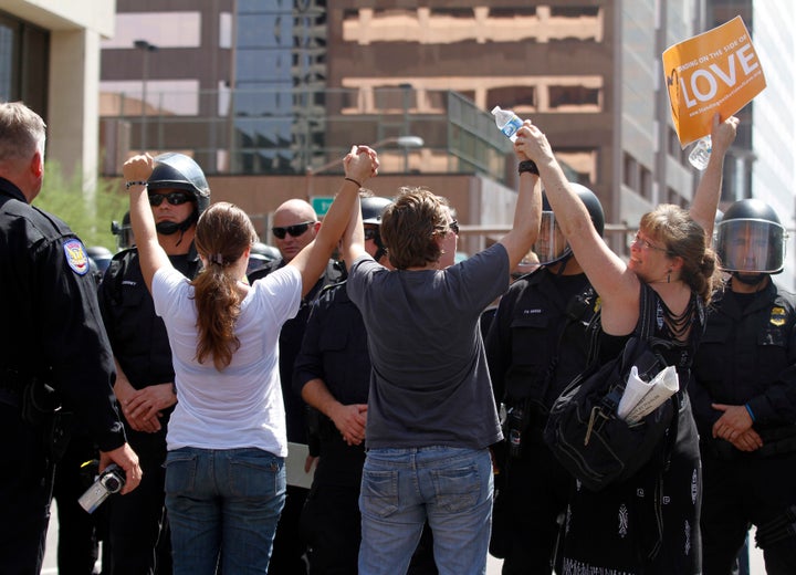 Demonstrators sand in front of riot police with their arms in the air during a protest against Arizona's controversial Senate