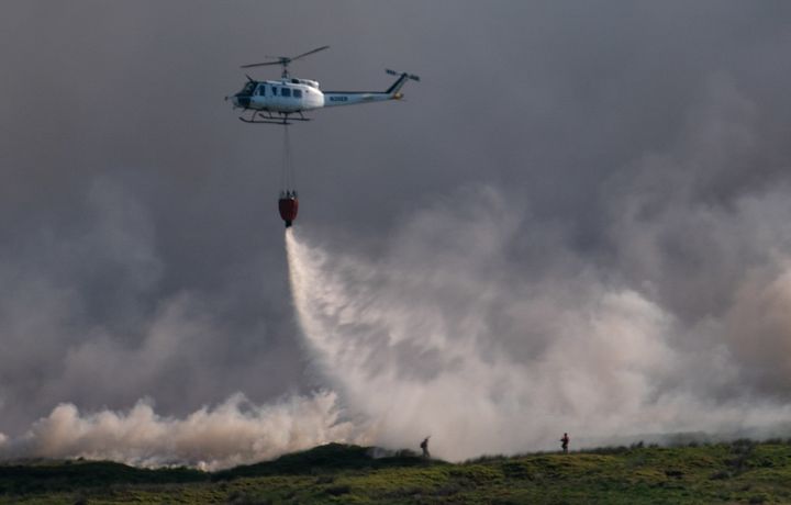A helicopter drops water on the grass fire enveloping Winter Hill near Bolton on June 30, 2018 in Bolton, England.