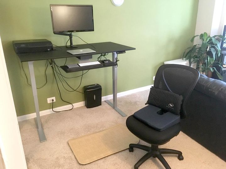 Lunkenheimer's workstation outfitted to help manage his pain with a sit-to-stand desk with raised monitor for correct position, left-hand trackpad for scrolling up and down, right-hand mouse for clicking, and anti-fatigue pad for standing. If sitting, he uses an ergonomic chair with wedge pillow to raise his hips above his knees and an inflatable pillow for lumbar support.