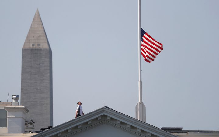 A worker looks up after lowering the flag over the White House in Washington to half-staff to honor victims of the shooting at the Capital Gazette Newspaper.