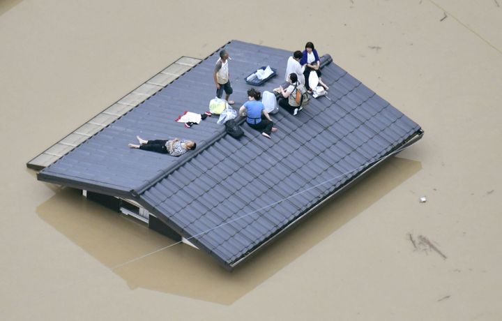 An aerial view shows local residents on the roof of a submerged house in a flooded area as they wait to be rescued in Kurashiki, Okayama Prefecture, on July 7, 2018.