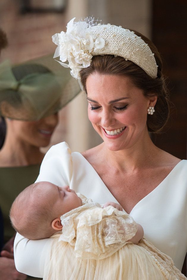 The Duchess of Cambridge holding Prince Louis, with Meghan, Duchess of Sussex in the background. 