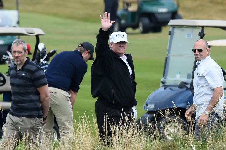 US President Donald Trump waves to protesters as he enjoy a round of golf as Turnberry