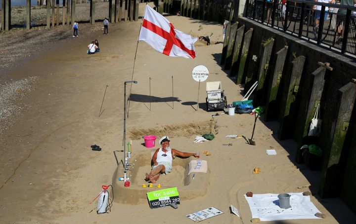 A man sits on the sand of a beach revealed by a low tide of the River Thames.