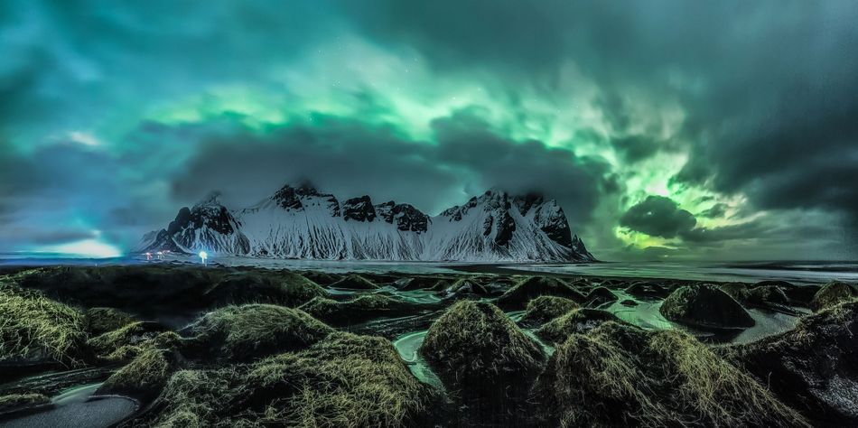 The magical Aurora Borealis explodes from the clouds and looms over the mountains in Stokknes on the south coast of Iceland Snow has melted and created pools of water between the dunes creating a perfect foreground for this image Stokksnes Iceland 16 February 2018