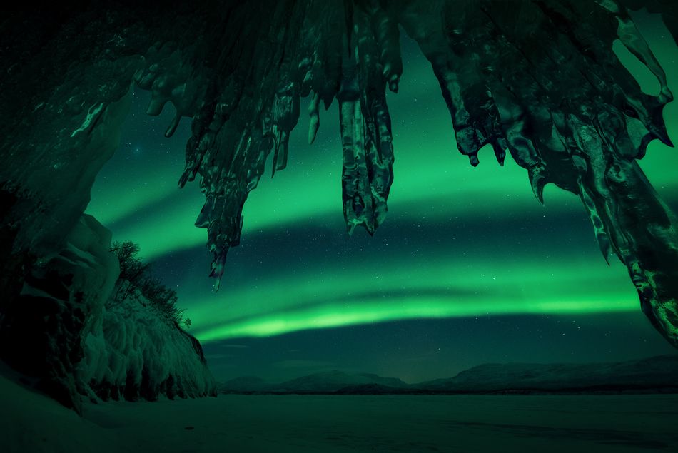 A remarkable display of the Northern Lights reflecting shades of green and yellow on the snow Squeezed into a tiny cave on Lake Tornetrask in Swedish Lapland in minus 26 degrees with the camera lens just a few centimeters away from the icicles it was a challenge well worth it for the photographer Abisko Sweden 18 February 2018