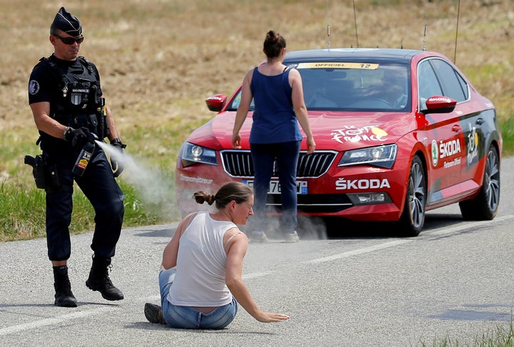 A police officer pepper-sprays a protester as another protester stands in front of the race director's car. The farmers were
