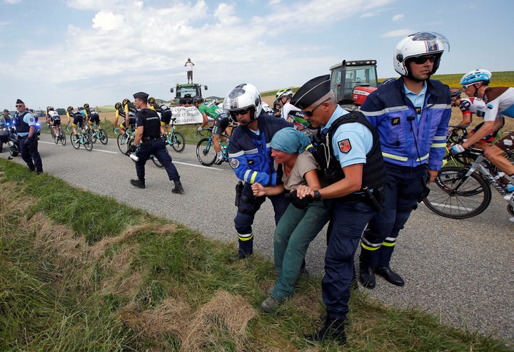 Police officers carry a protester off the road on Tuesday as cyclists with the Tour de France pass.