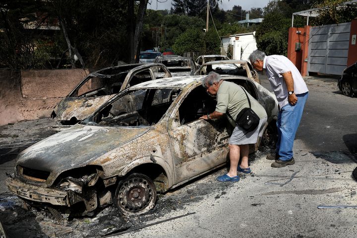 People look inside a burnt car following a wildfire at the village of Mati, near Athens, Greece.