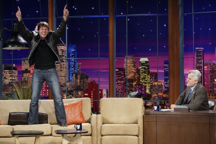 Tom Cruise stands on a couch, something he likes to do, during an interview on