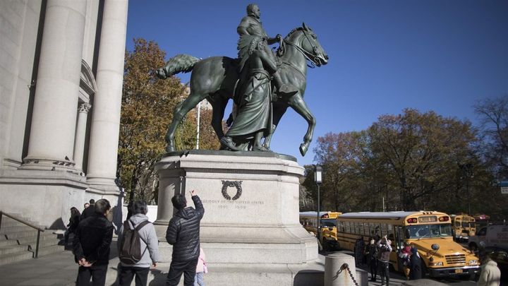 Visitors to the American Museum of Natural History look at a statue of Theodore Roosevelt, which includes a man in a Native American headdress. A mayoral commission couldn’t decide whether the statue is racist.