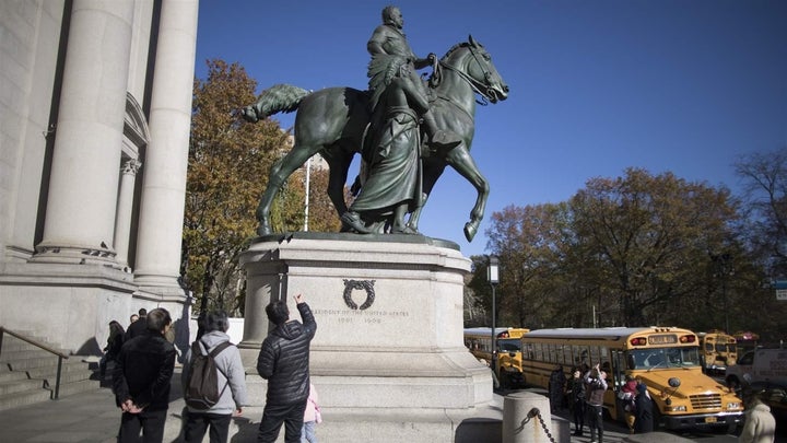 Visitors to the American Museum of Natural History look at a statue of Theodore Roosevelt, which includes a man in a Native A