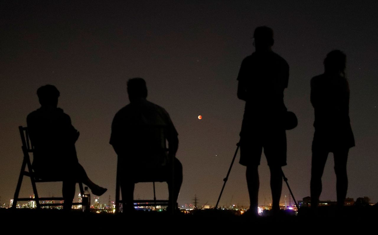 People in a field watch the moon over the skyline of Frankfurt, Germany.