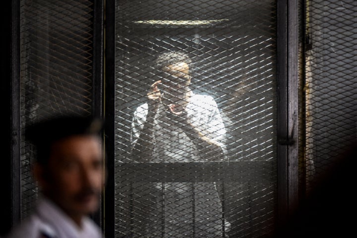 Egyptian photojournalist Mahmoud Abdel Shakour Abouzied, also known as Shawkan, makes a gesture mimicking taking a photograph from inside a soundproof glass dock, during his trial in the capital Cairo on July 28, 2018.