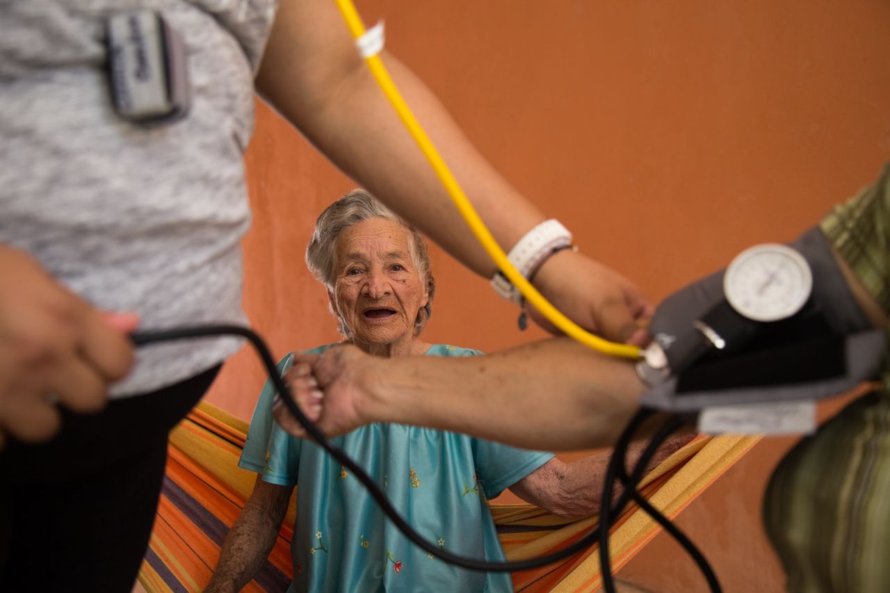 Abdona Villonueva suffers from dementia and Alzheimer's but still happily spends her time swinging on her hammock in her home in Aguada. She is cared for by her daughter Carmen who is having her blood pressure checked while Abdona watches.