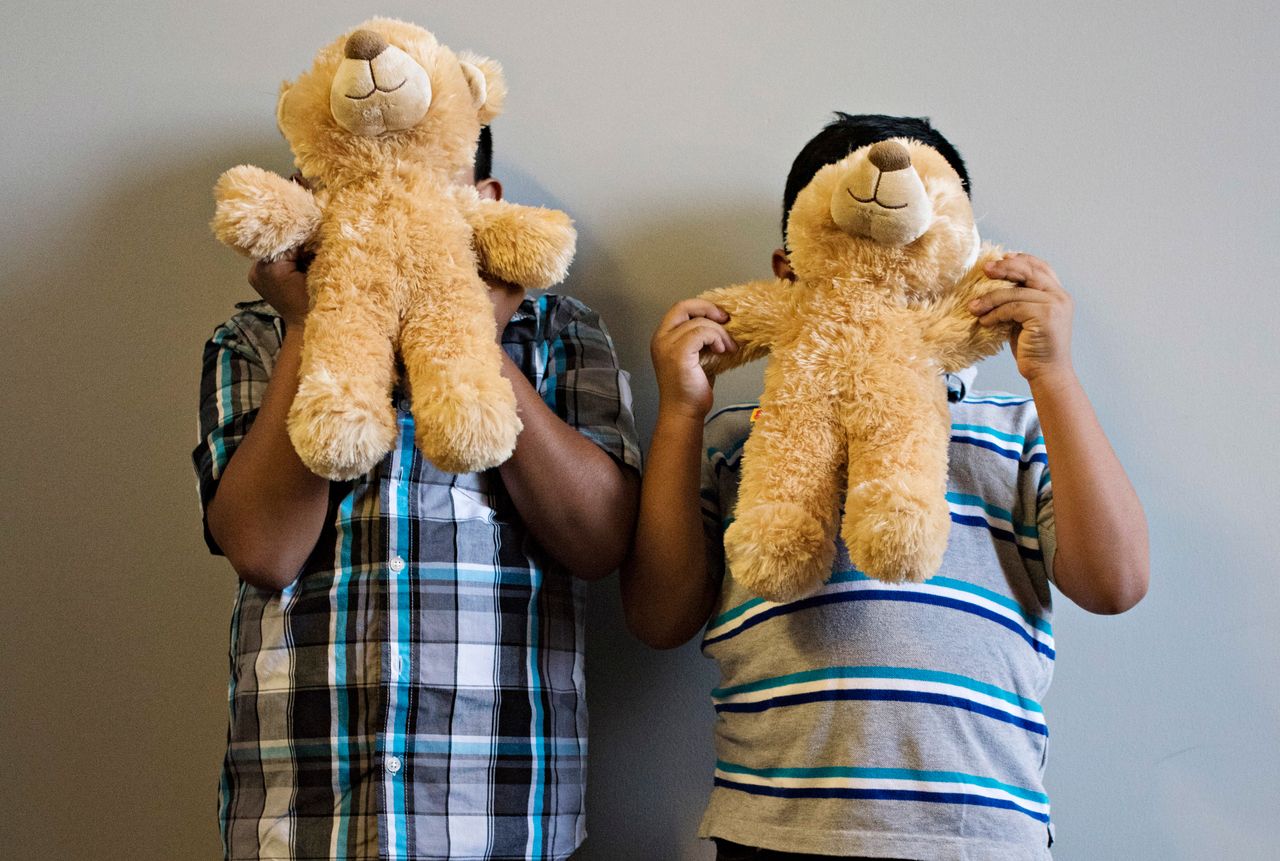 Luis and Jorge hold up teddy bears in front of their faces. 
