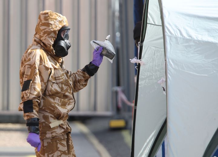 An investigator in a chemical suit removes items as they work behind screens erected in Salisbury, Wiltshire.