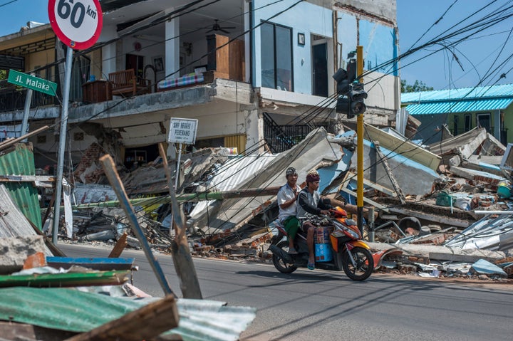 Motorists ride past buildings ruined by Sunday's earthquake in Pamenang, Lombok Island, Indonesia, Friday, Aug. 10, 2018. The north of the popular resort island has been devastated by Sunday's earthquake, damaging thousands of buildings and killing a large number of people.