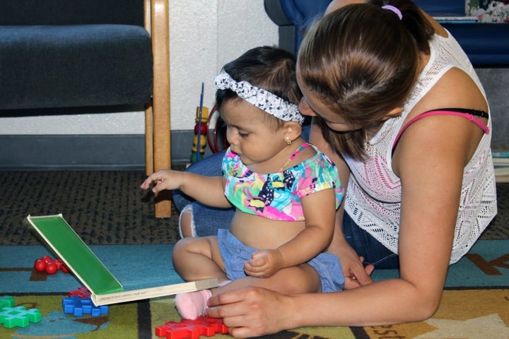 An infant stares at the colorful images in an alphabet board book as her mother reads to her after a summer storytime at Cesar Chavez Public Library in Oakland, Calif.