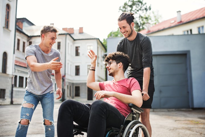 A disabled boy in wheelchair with two teenager friends outside having fun in town.