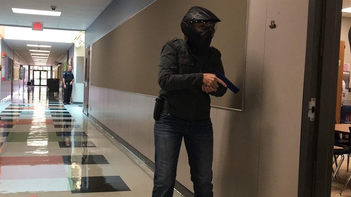 A school marshal trainee, wearing protective headgear, cautiously approaches a classroom in a simulated search for an armed i