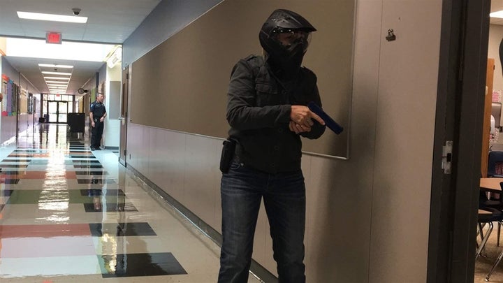 A school marshal trainee, wearing protective headgear, cautiously approaches a classroom in a simulated search for an armed intruder. School marshals carry concealed weapons, undergo training and psychological evaluations and often work with school resource officers to guard against potential threats. 