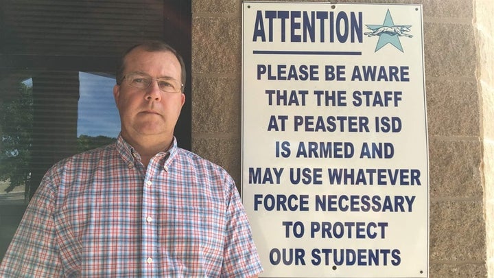 Matt Adams, superintendent of the Peaster Independent School District in Parker County, Texas, stands next to a sign intended to deter would-be intruders that is posted outside of the school. Several other Texas districts also have posted similar signs. 