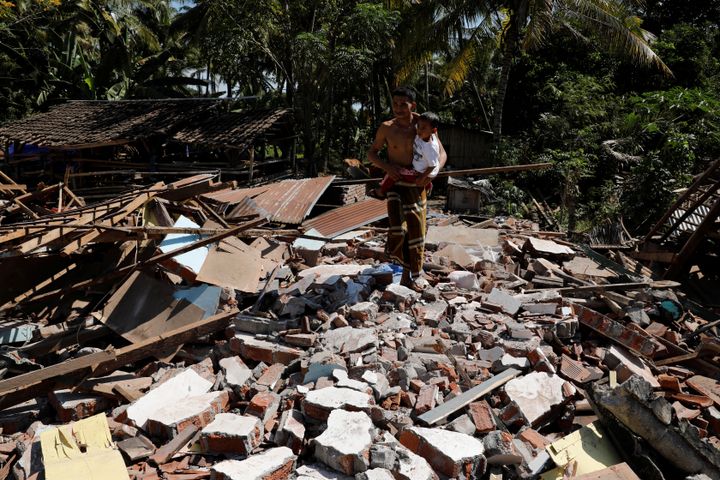 A man holds his child as he walks through the ruins of their house at Kayangan district after an earthquake hit on August 5 in North Lombok, Indonesia.