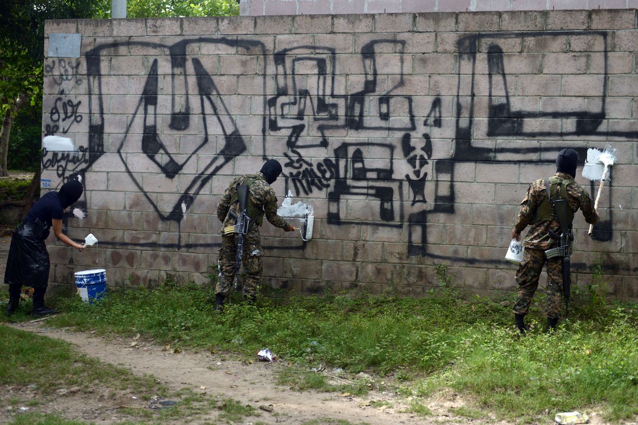 Police officers and soldiers paint over graffiti associated with the Mara Salvatrucha gang, or MS-13, in Quezaltepeque, El Salvador.